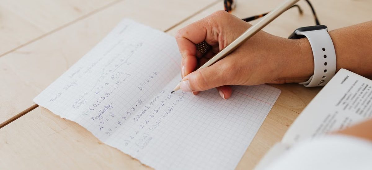 A close-up of a person writing mathematical equations on graph paper with a pencil.