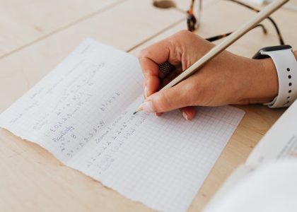 A close-up of a person writing mathematical equations on graph paper with a pencil.